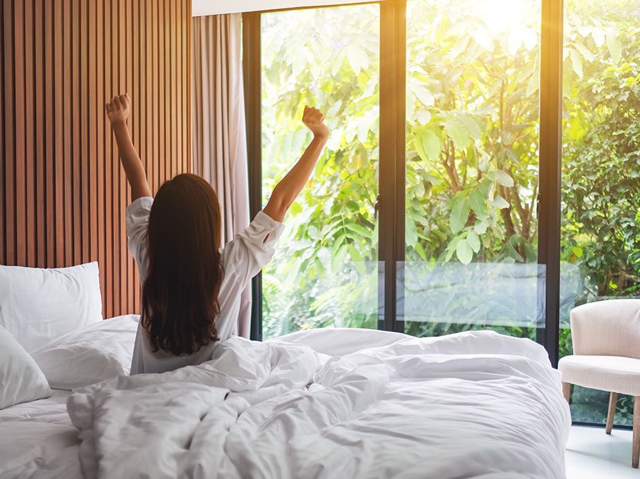Woman waking up in bed with sun shining through windows.